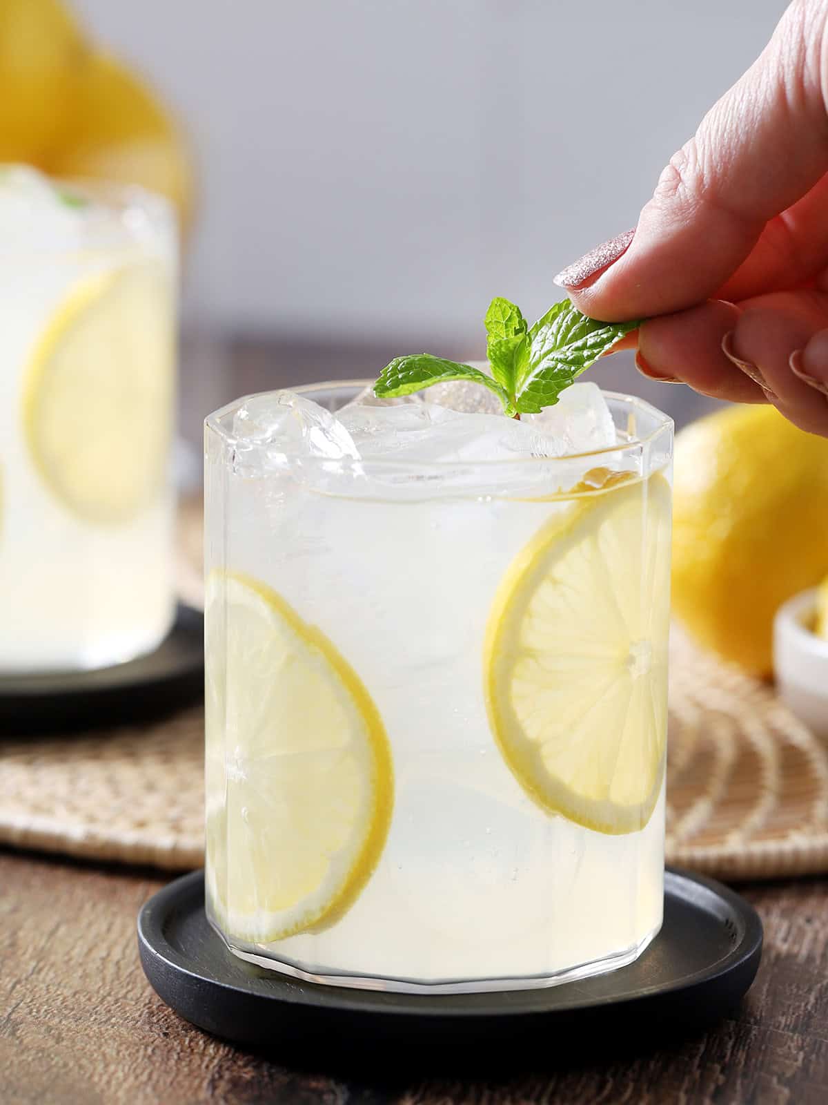 A hand placing a mint sprig garnish onto a glass of lemonade.