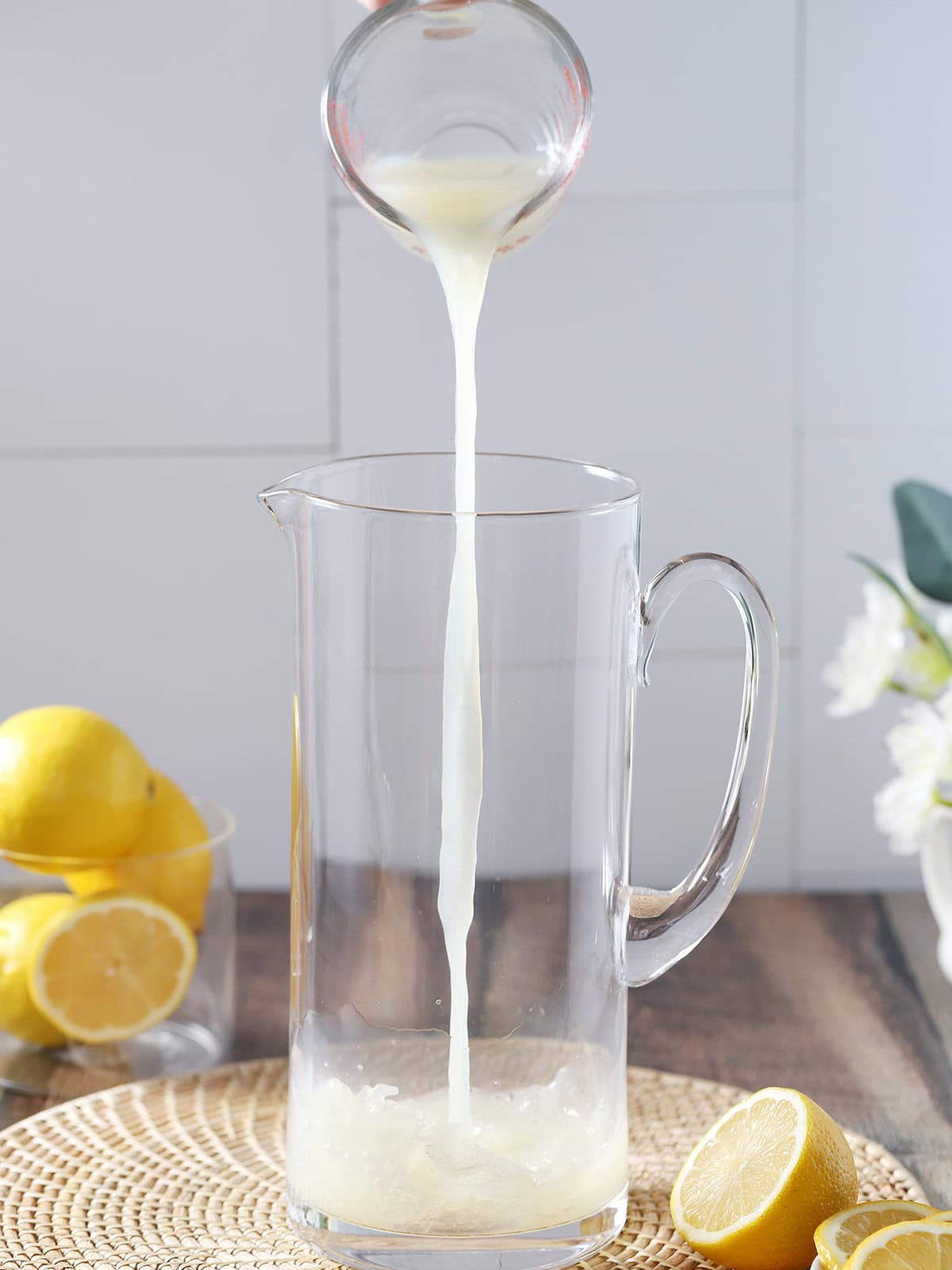 Lemon juice being poured into a tall glass pitcher.