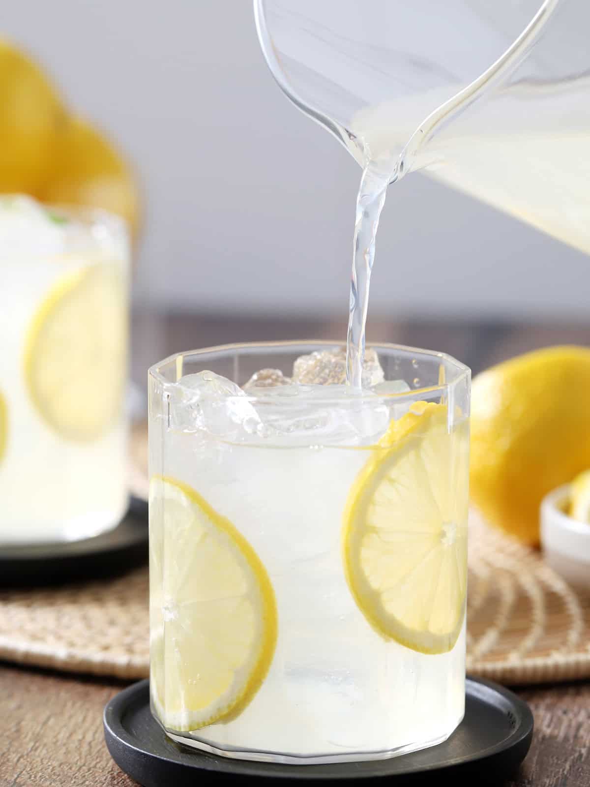 Lemonade being poured from a glass pitcher into a glass of ice.
