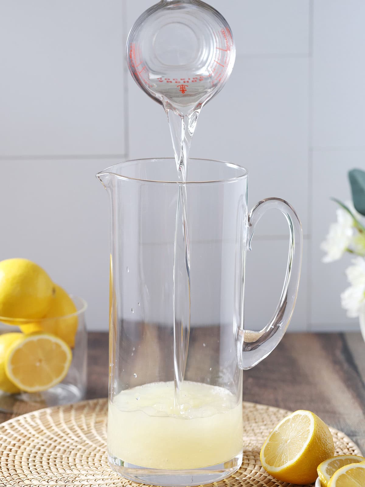 Simple syrup being poured into a pitcher of lemon juice.