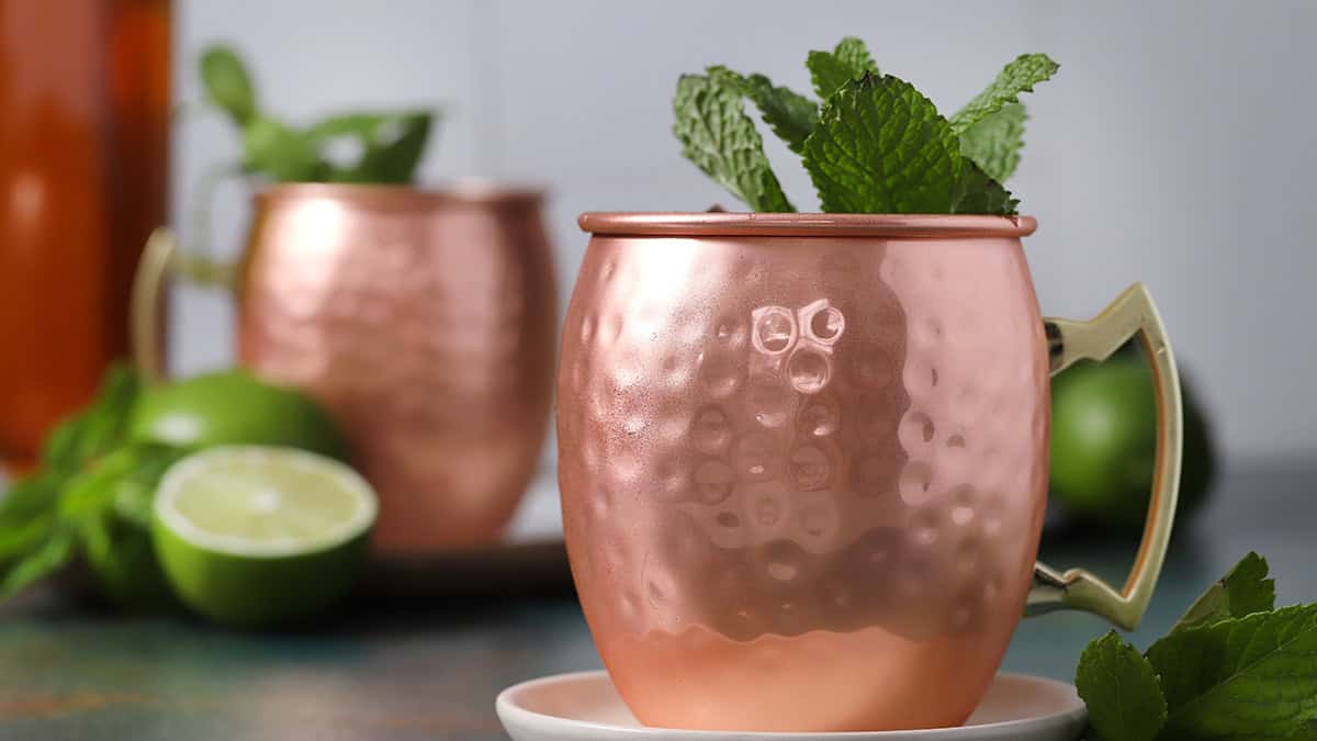 Two copper mugs filled with Kentucky mule cocktails garnished with fresh mint and limes.