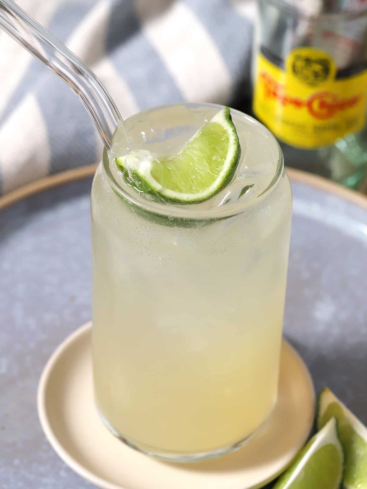 A glass of ranch water surrounded by bottles of Topo Chico and garnished with fresh lime.