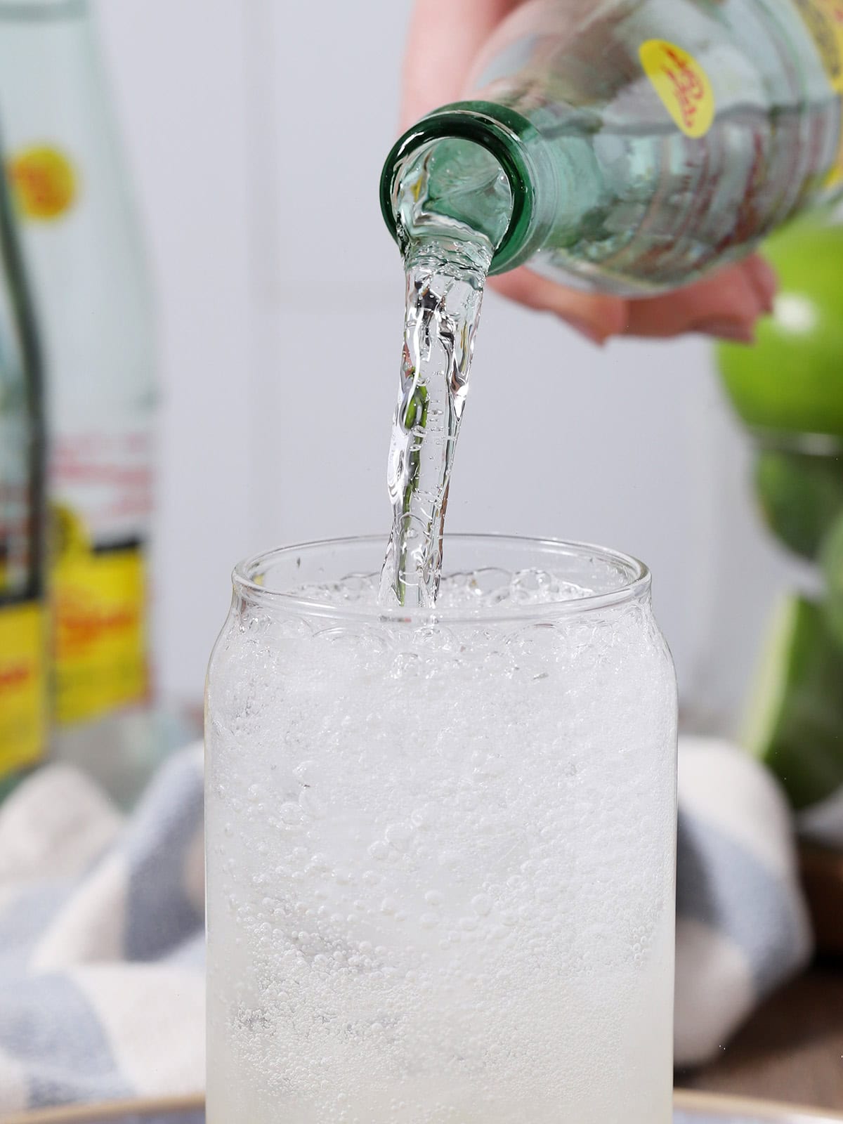 A hand pouring mineral water from a bottle into a glass of ranch water. 