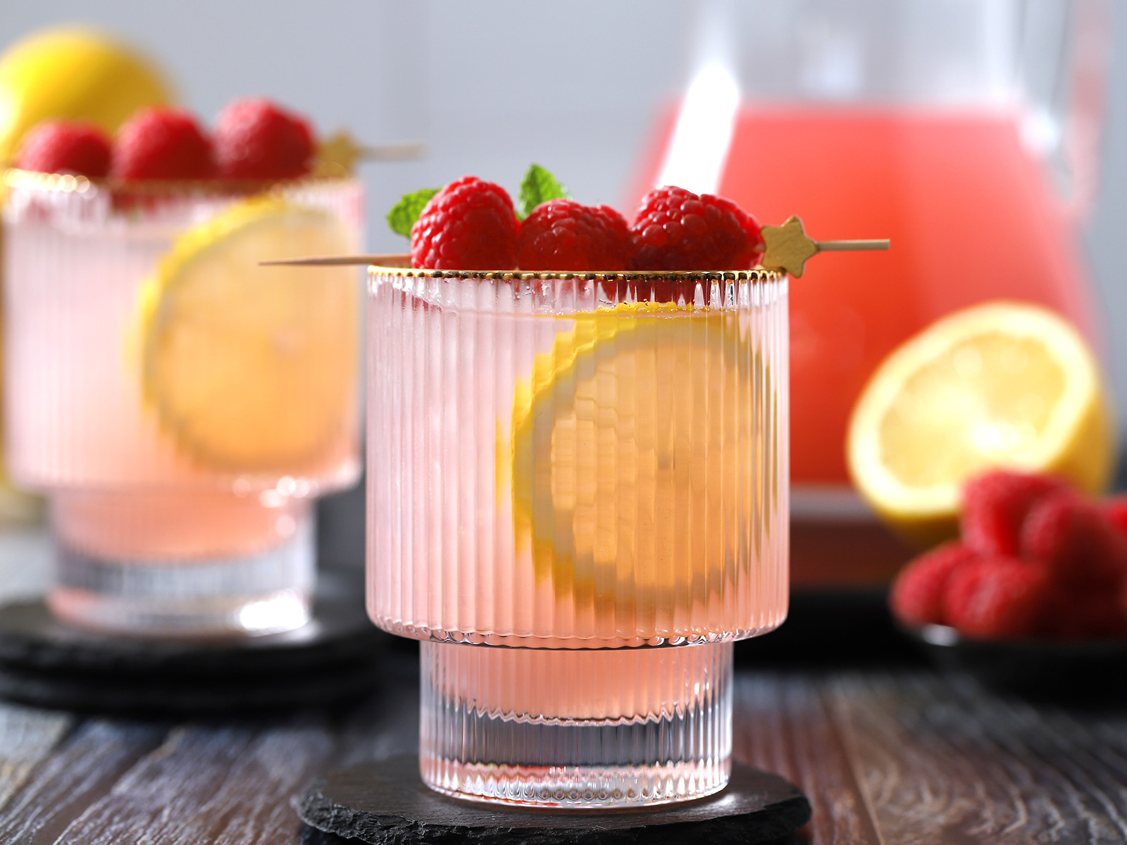 Glasses of raspberry lemonade, garnished with large slices of lemon and fresh raspberries.