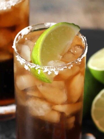 A glass of batanga cocktail garnished with a lime wedge and salted rim.