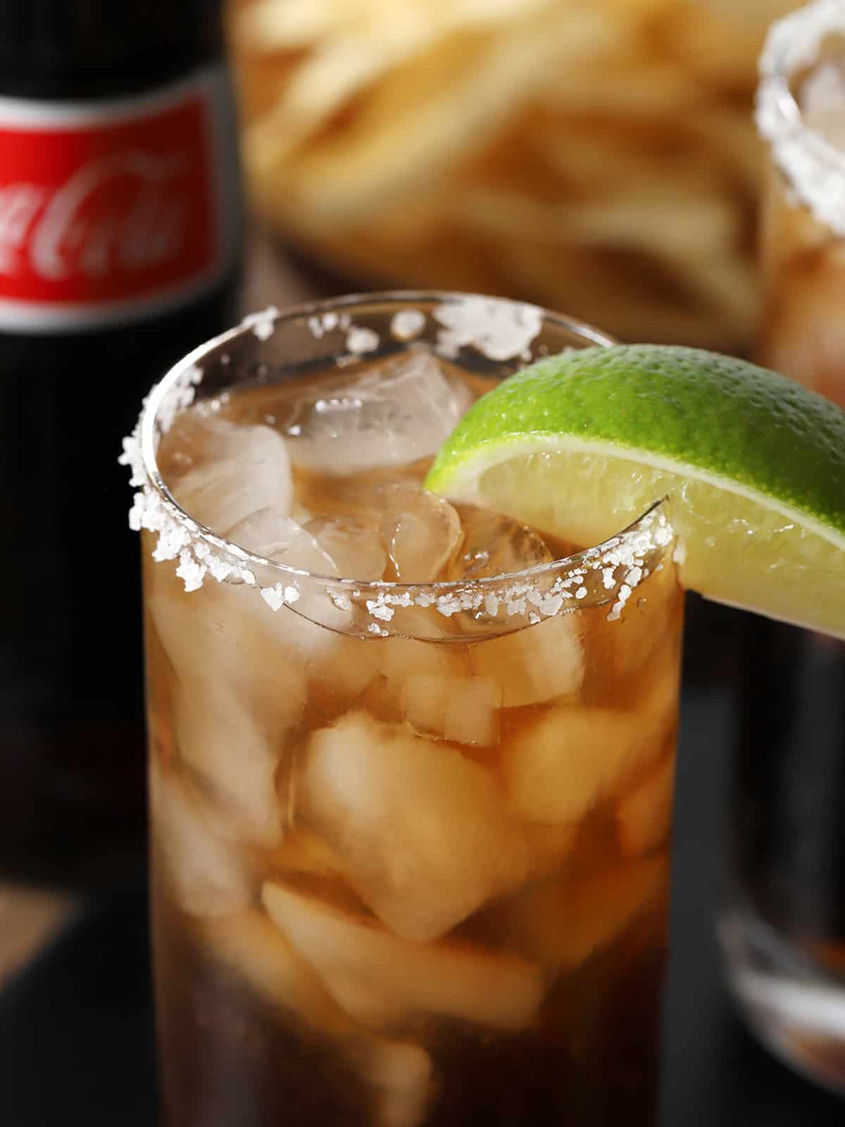 A glass of batanga cocktail garnished with a lime wedge and salted rim.