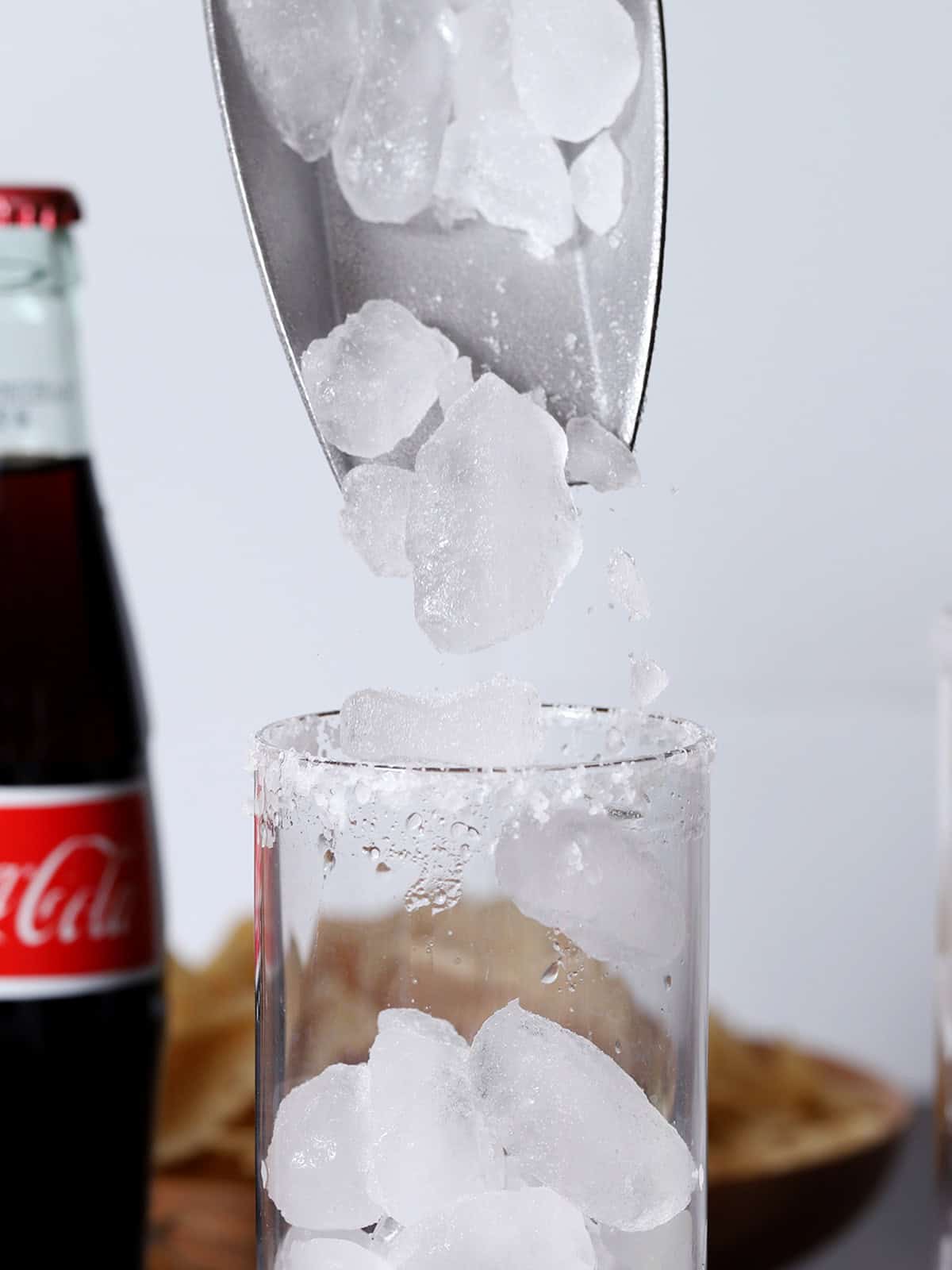Ice cubes dropping from a silver scoop into a tall glass.