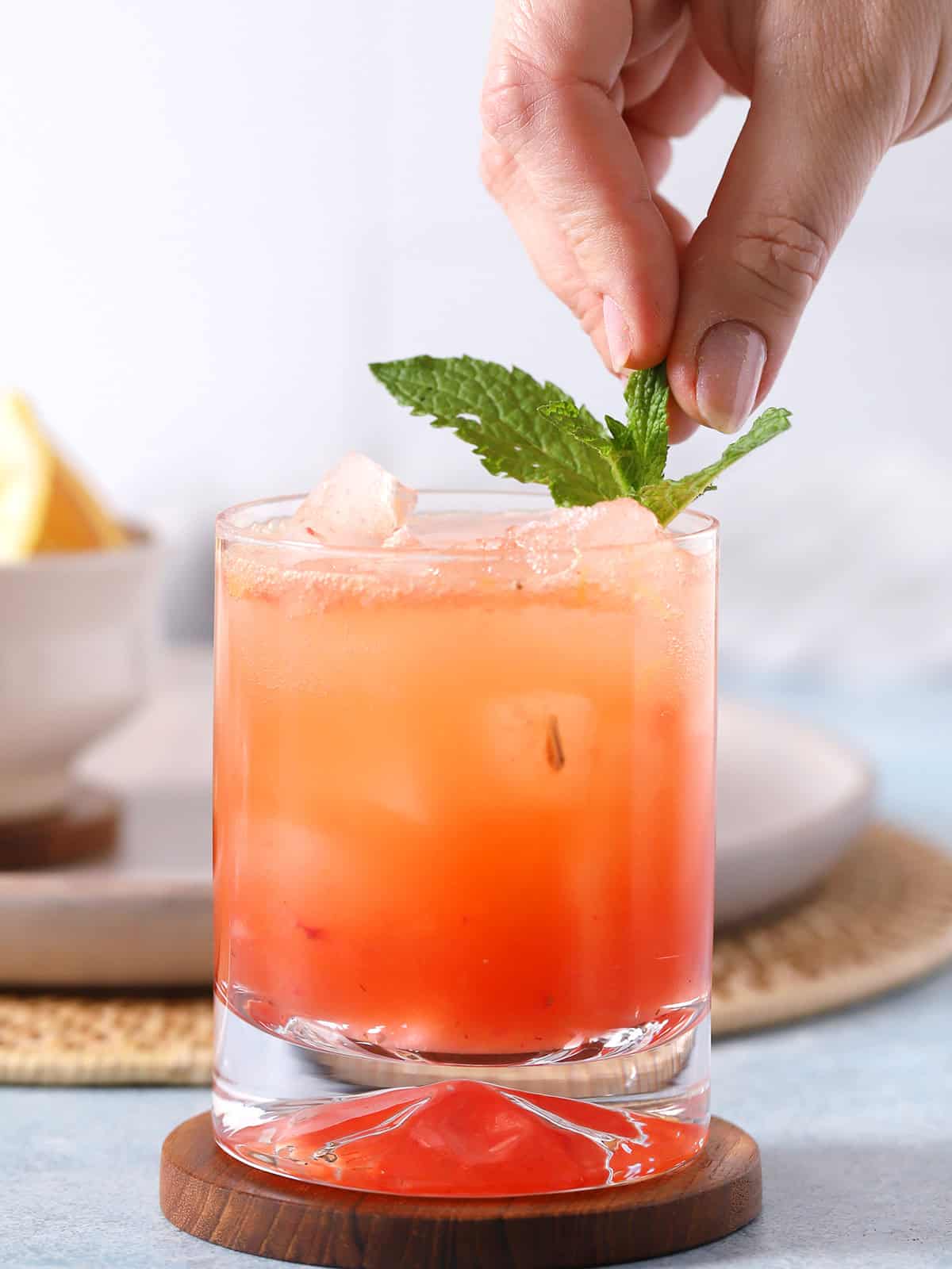 A hand placing a piece of mint into a glass of bourbon smash.