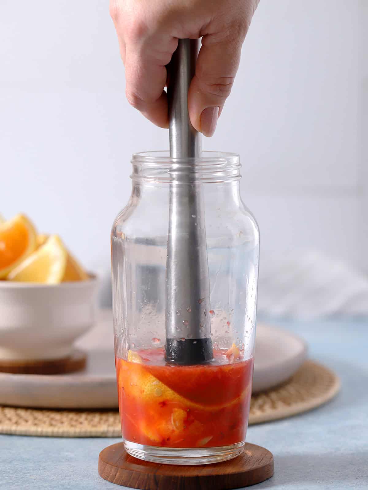 A hand pressing a muddler into a cocktail shaker full of fruit.