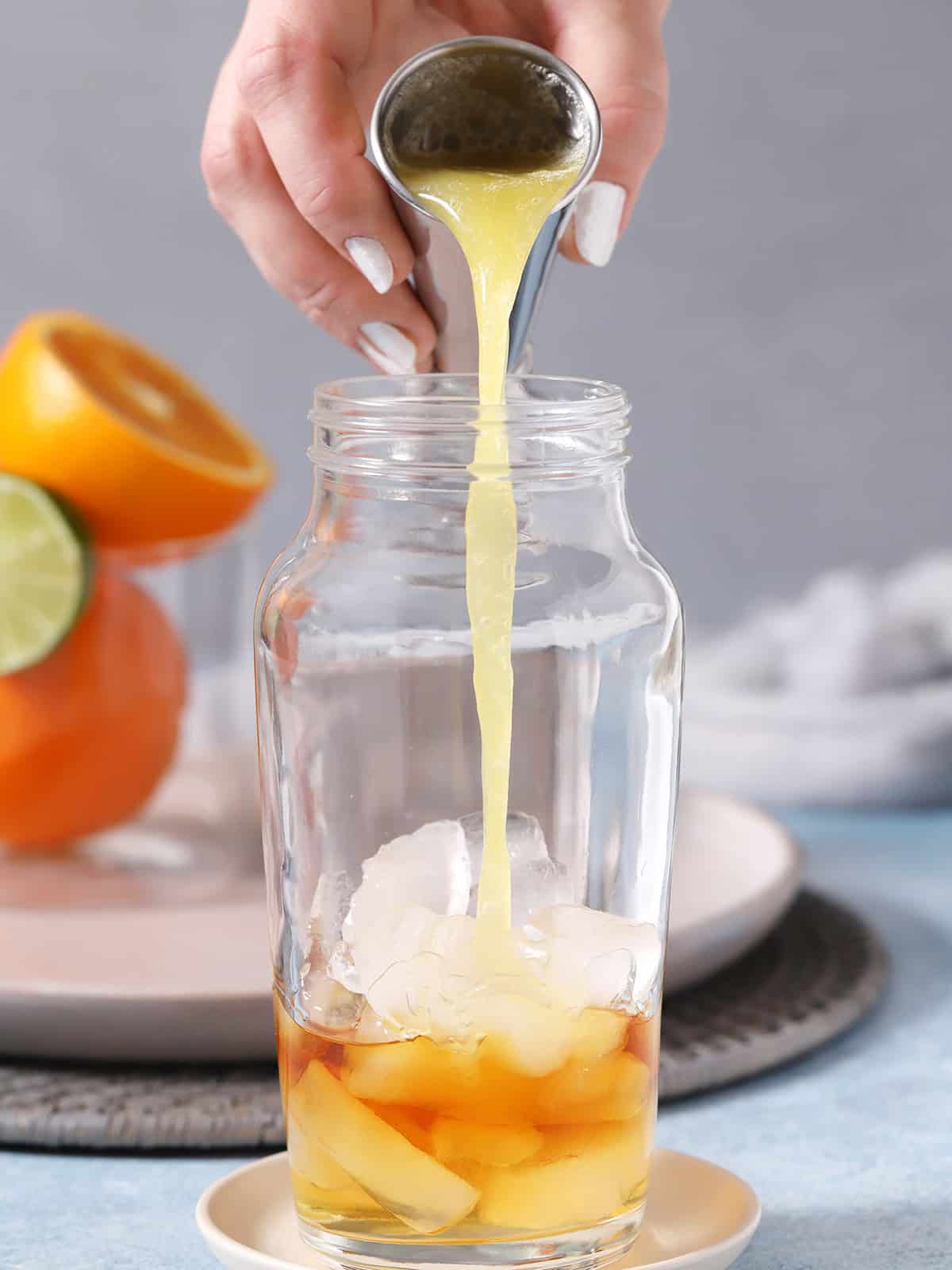 A hand pouring pineapple juice into a cocktail shaker filled with ice.