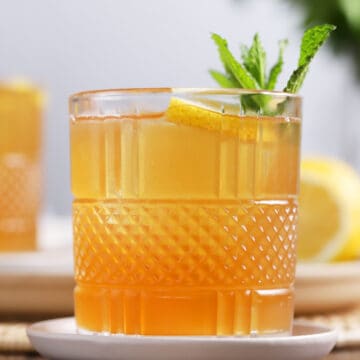 A glass of spiked arnold palmer cocktail garnished with lemon and mint.