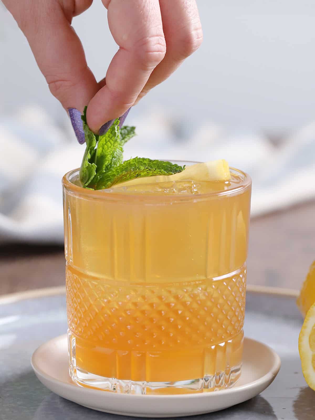 A hand placing a sprig of mint into a glass of Spiked Arnold Palmer cocktail.