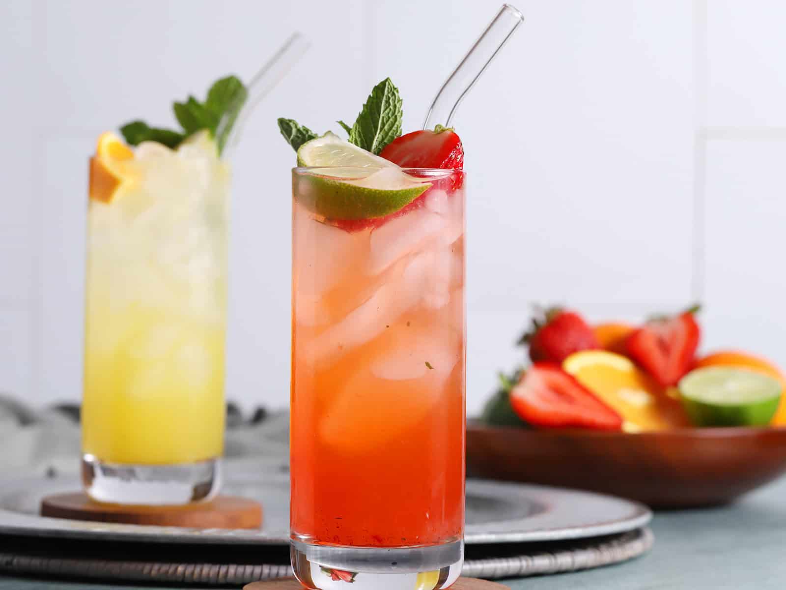 A tall glass of tequila smash cocktail garnished with a lime wedge, mint, and berries.
