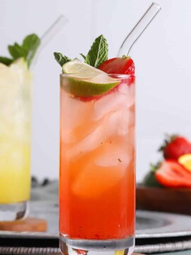 A tall glass of tequila smash cocktail garnished with a lime wedge, mint, and berries.