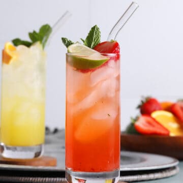 A tall glass of tequila smash cocktail garnished with a lime wedge, mint, and berries.