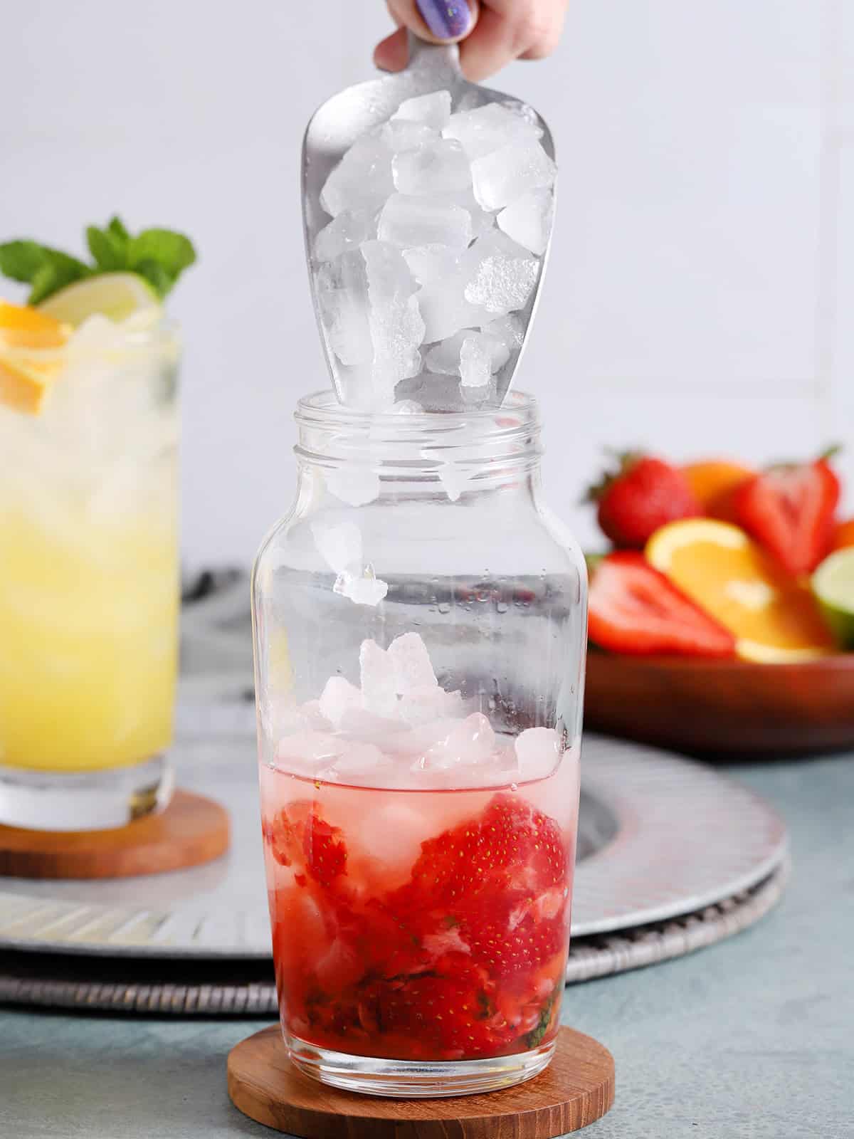 Ice being poured from a large scoop into a cocktail shaker.