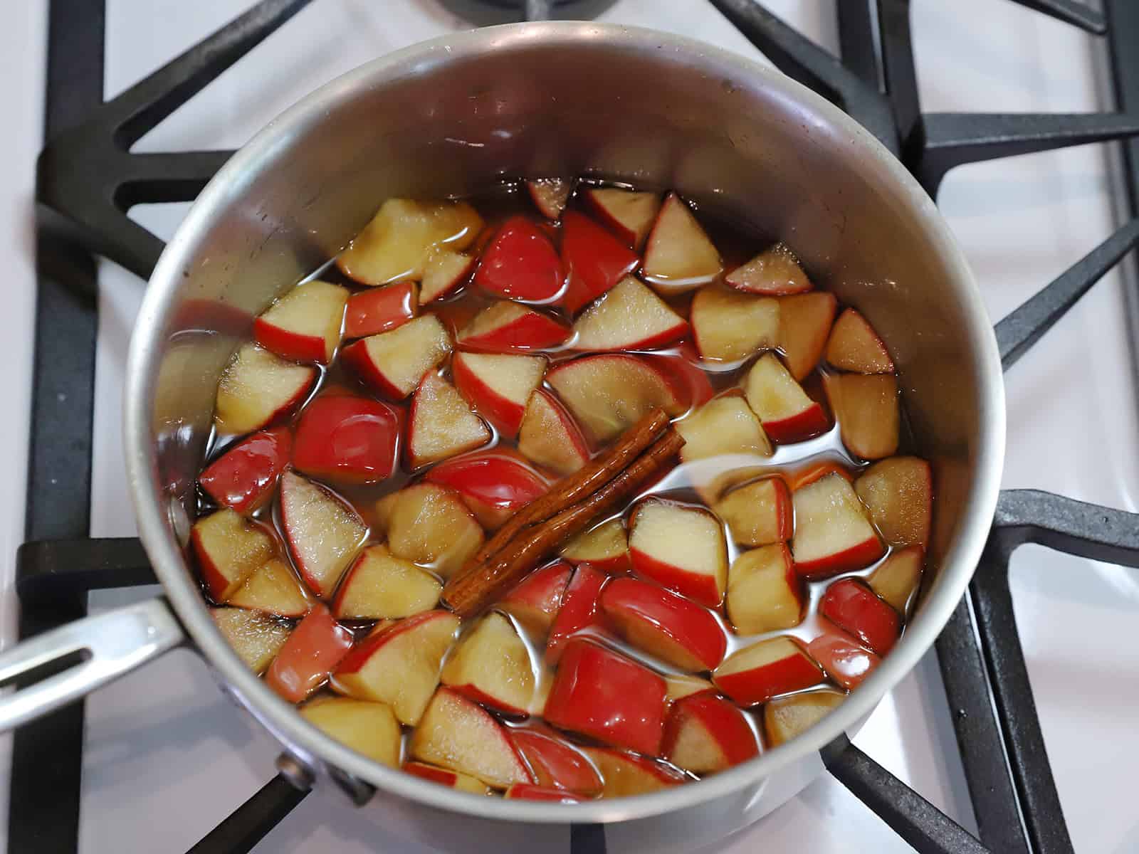 Cooked apples, syrup, vanilla, and cinnamon in a pot on the stove.