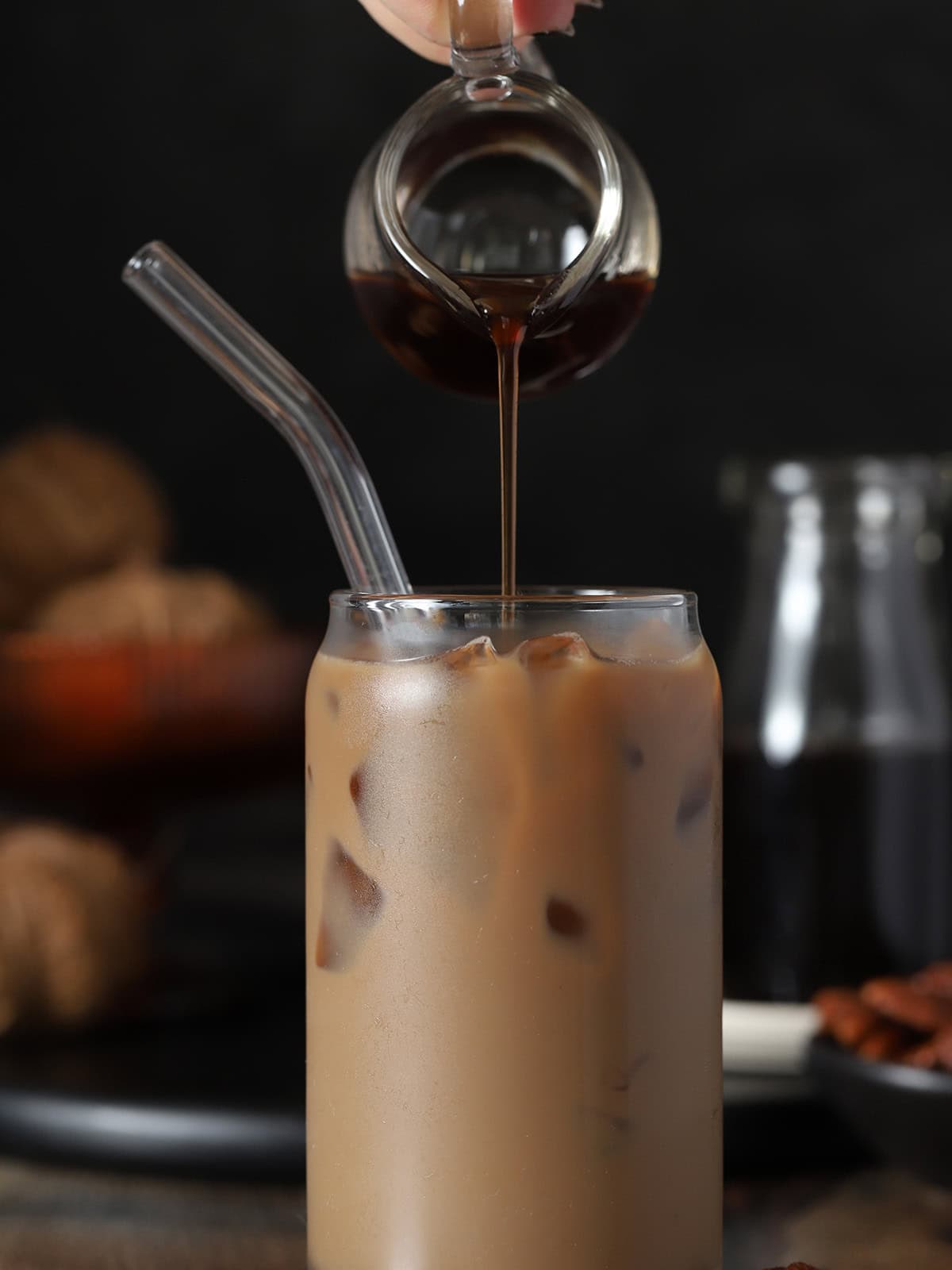 A hand pouring butter pecan syrup into an iced latte.