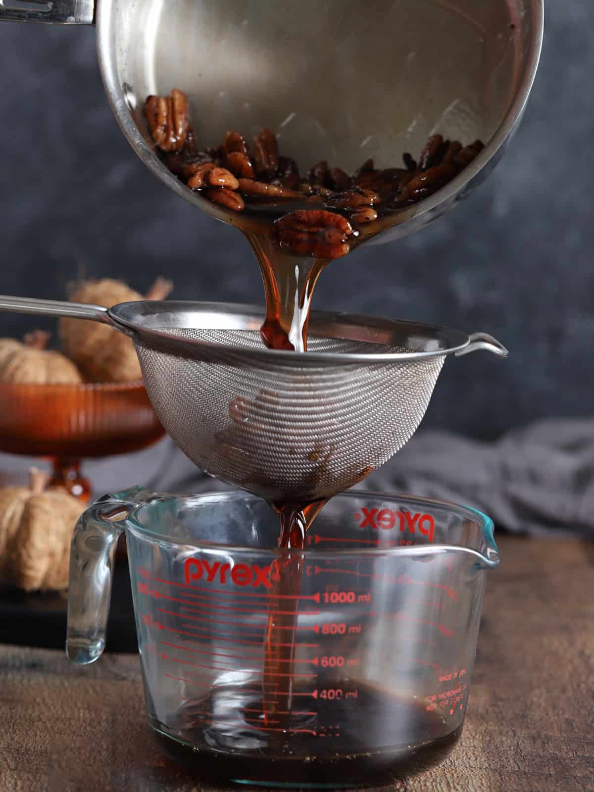 Syrup being poured through a fine mesh sieve held over a large measuring jar.
