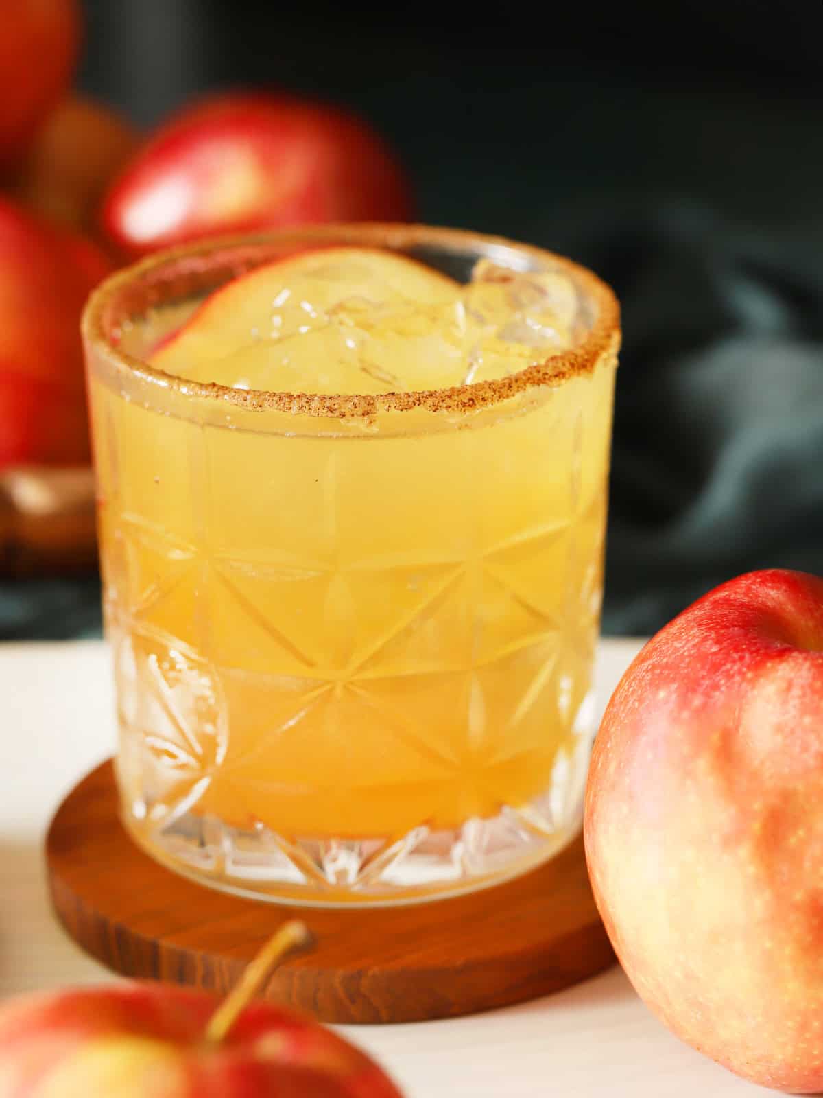 A glass filled with ginger apple cider mocktail, garnished with a slice with apple and a cinnamon sugar rim.