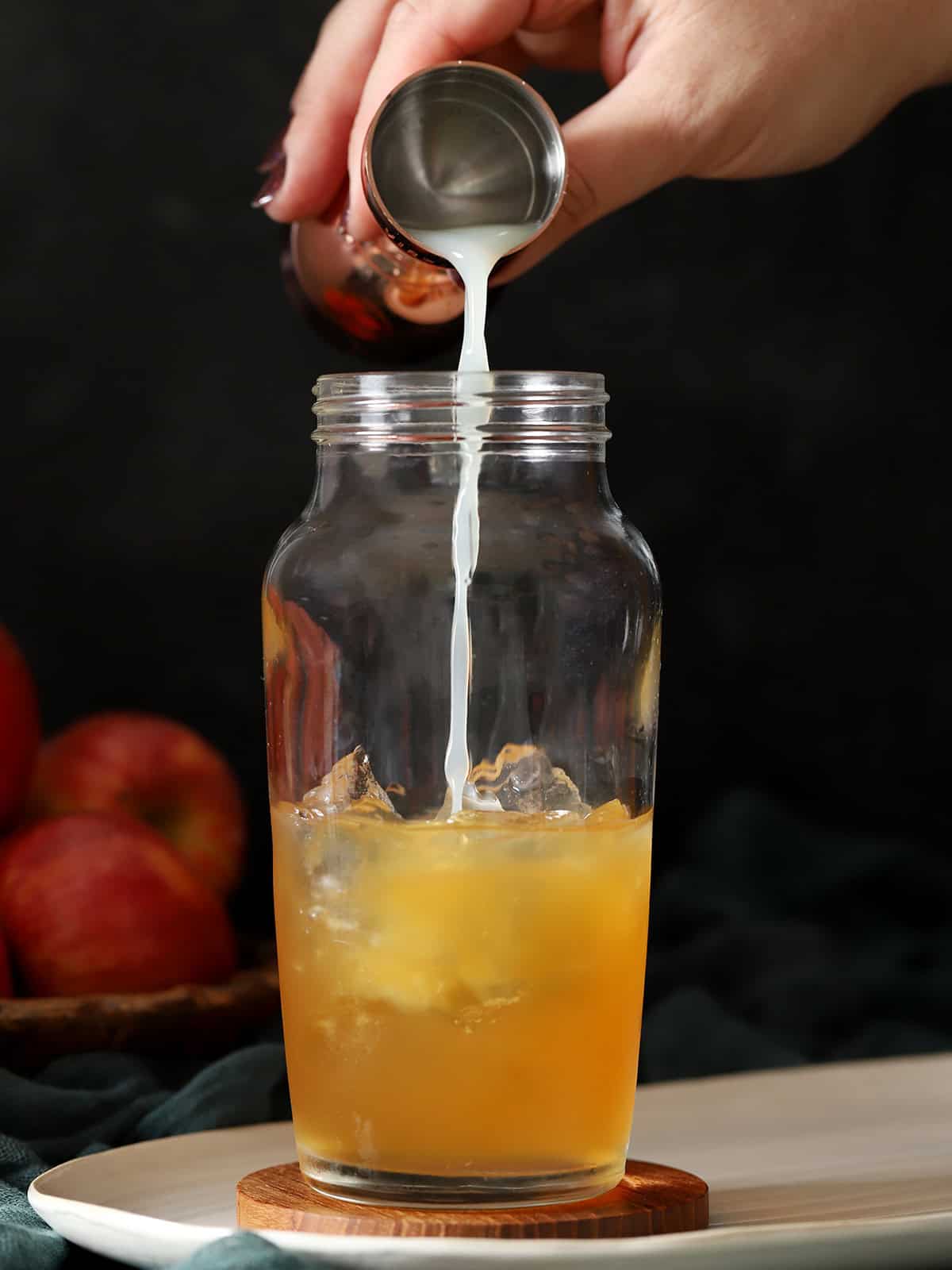 Lemon juice being poured into a cocktail shaker with apple cider and ice.