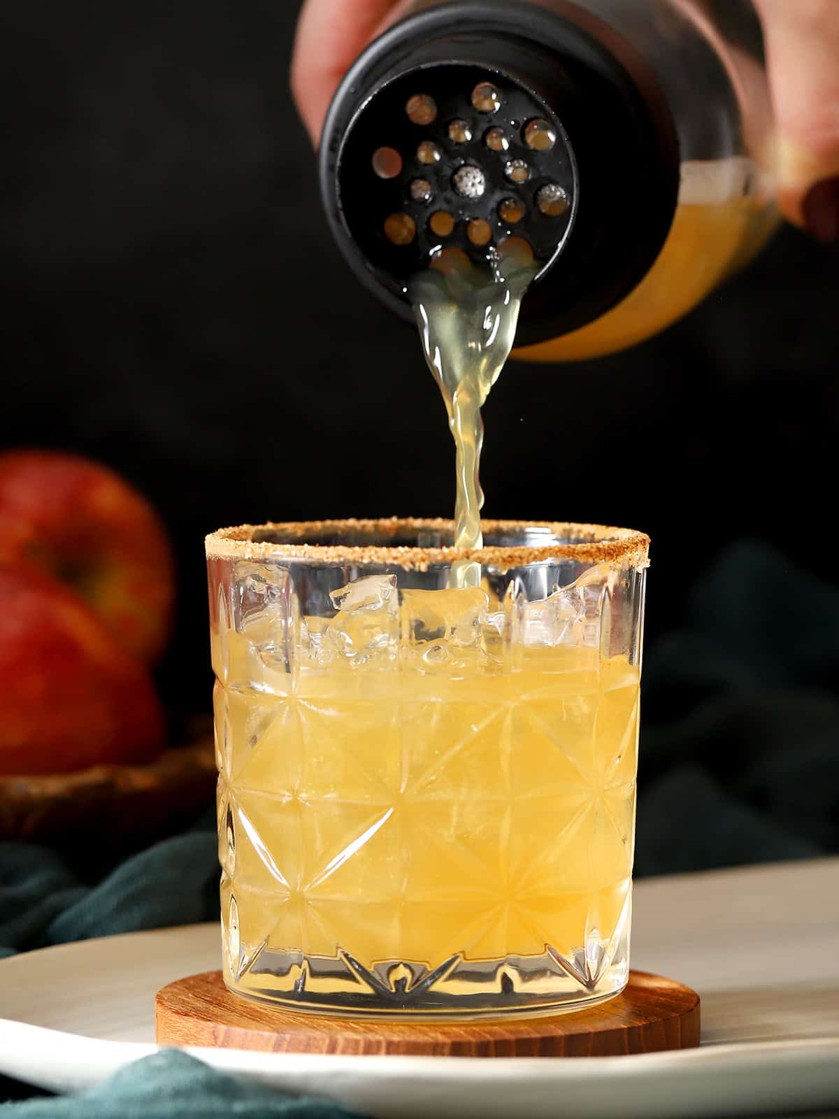 Apple cider mocktail being poured into a rocks glass filled with ice cubes.