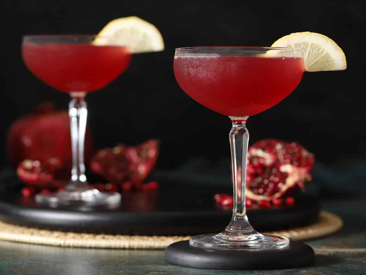 Glasses of pomegranate martinis garnished with slices of lemons.