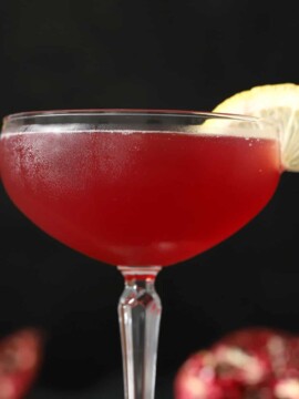 A glass of pomegranate martini garnished with a slice of lemon.