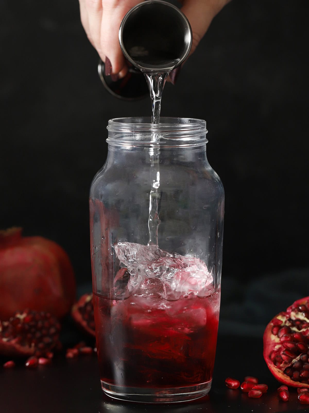 A hand pouring vodka into a cocktail shaker half-filled with ice cubes.