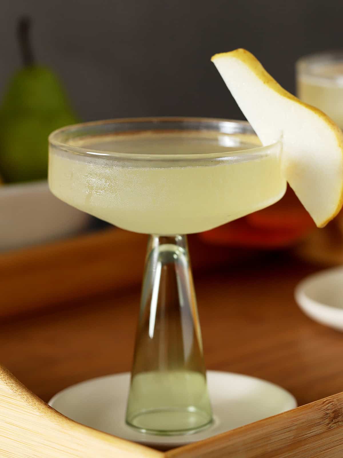 A coupe glass filled with pear martini, garnished with a slice of fresh pear.