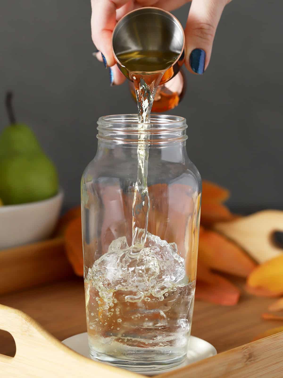 Pear juice being poured into a cocktail shaker half-filled with ice.
