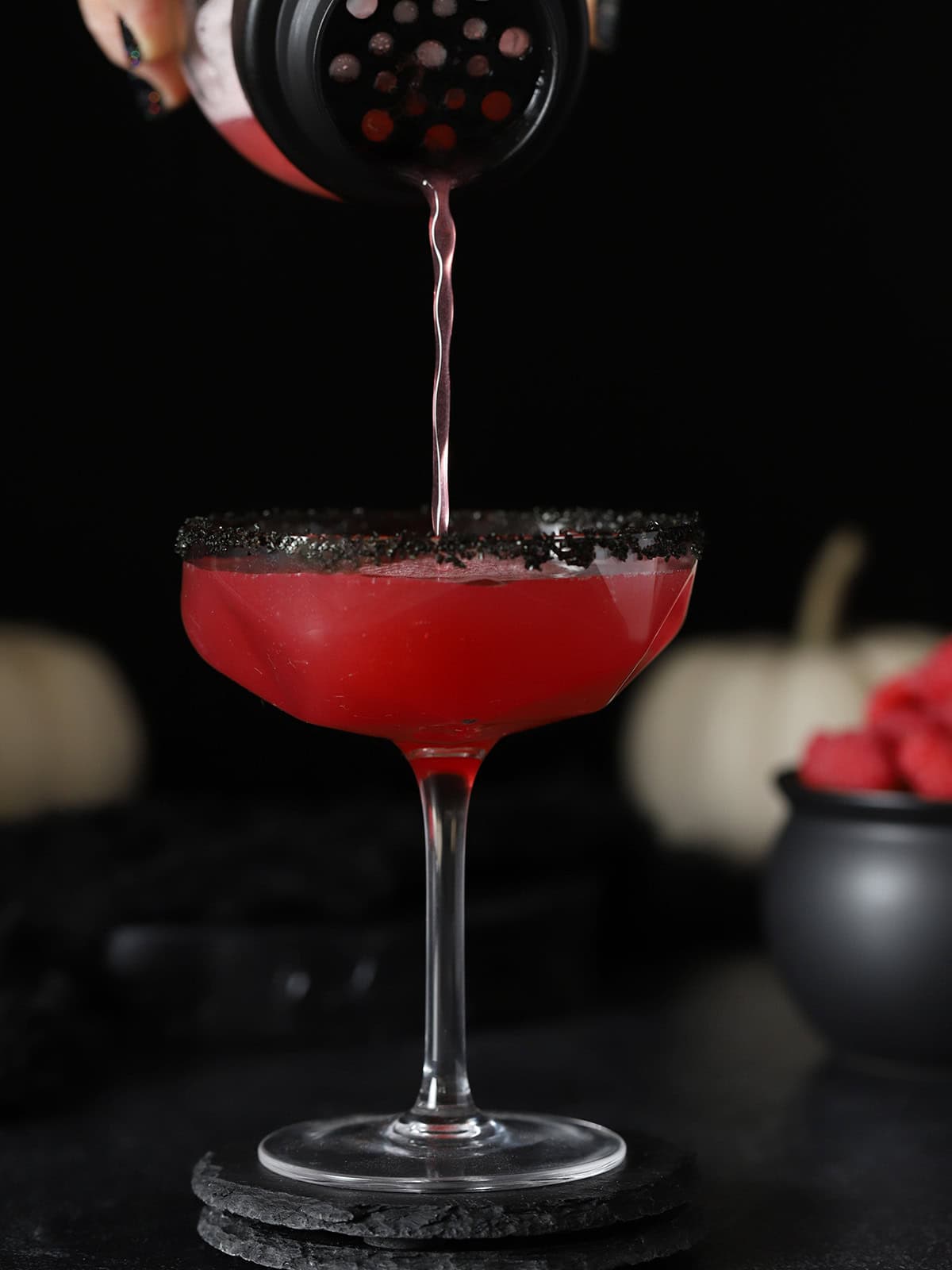 Vampire's Kiss Cocktail being poured from a cocktail shaker into a coupe glass with a black sugar rim.