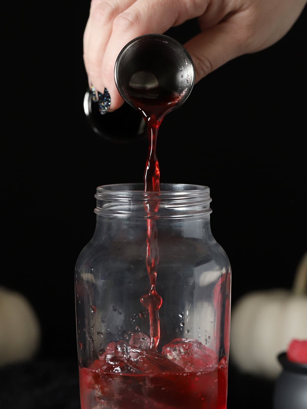A hand pouring cherry juice into a cocktail shaker.
