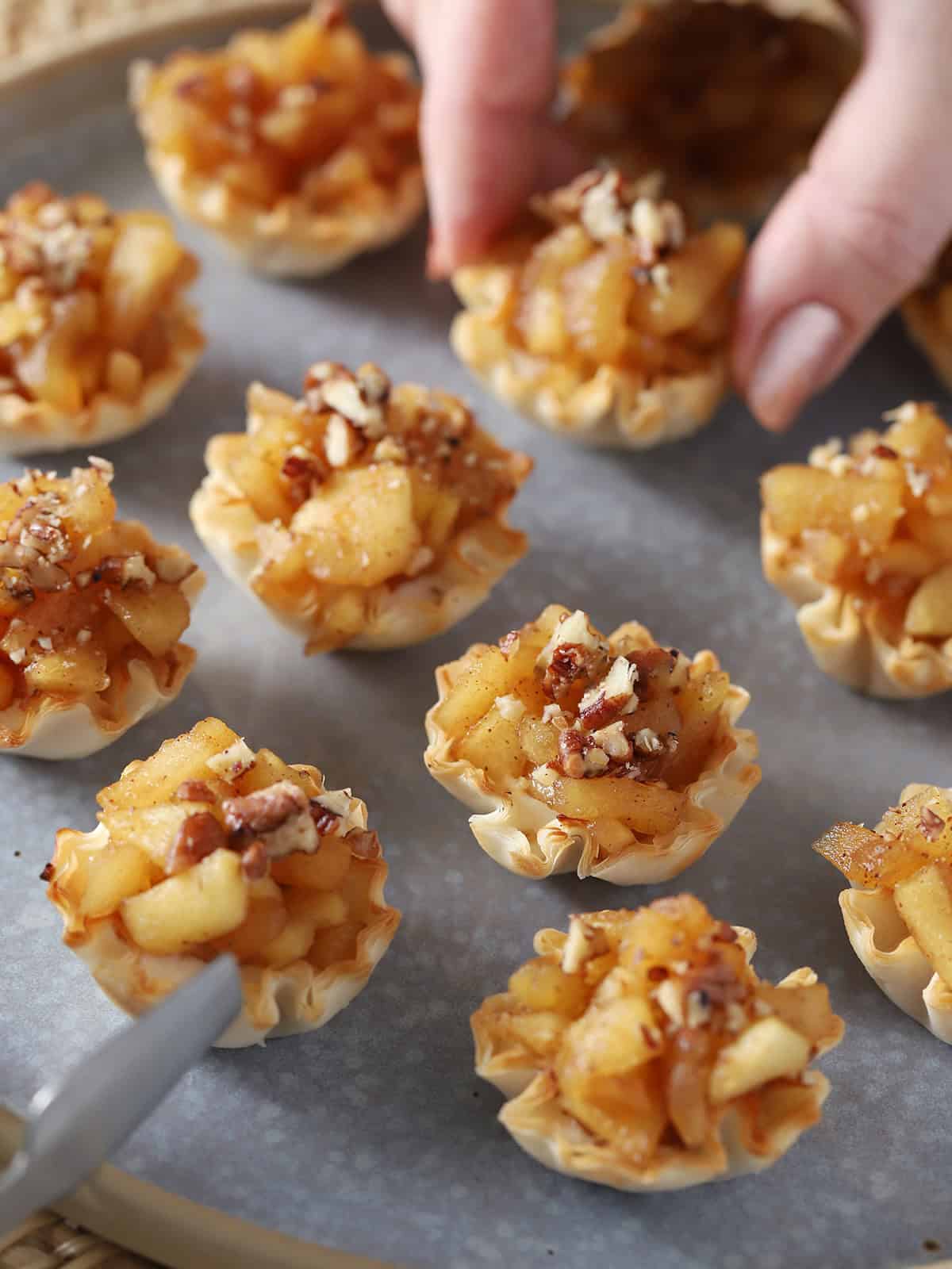 A hand picking up a mini apple pie bite.