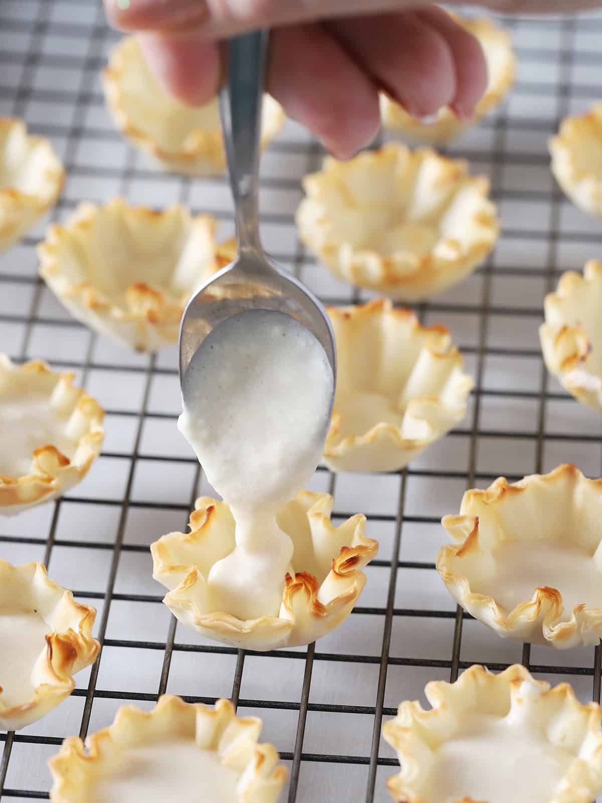 Spooning the cream cheese mixture into baked phyllo cups.