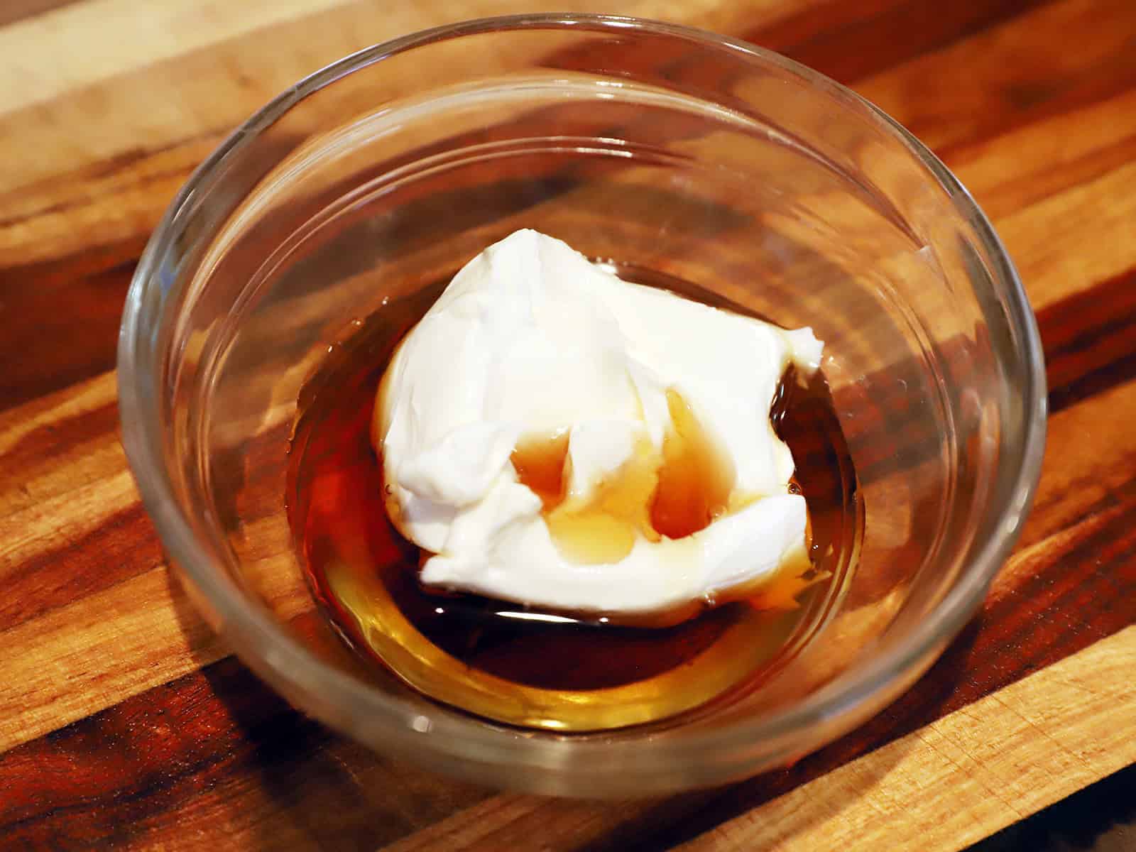 Cream cheese and maple syrup in a glass bowl on a wood table.