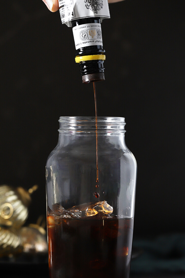 Bitters being added to a cocktail shaker filled with Gingerbread Espresso Martini cocktail.