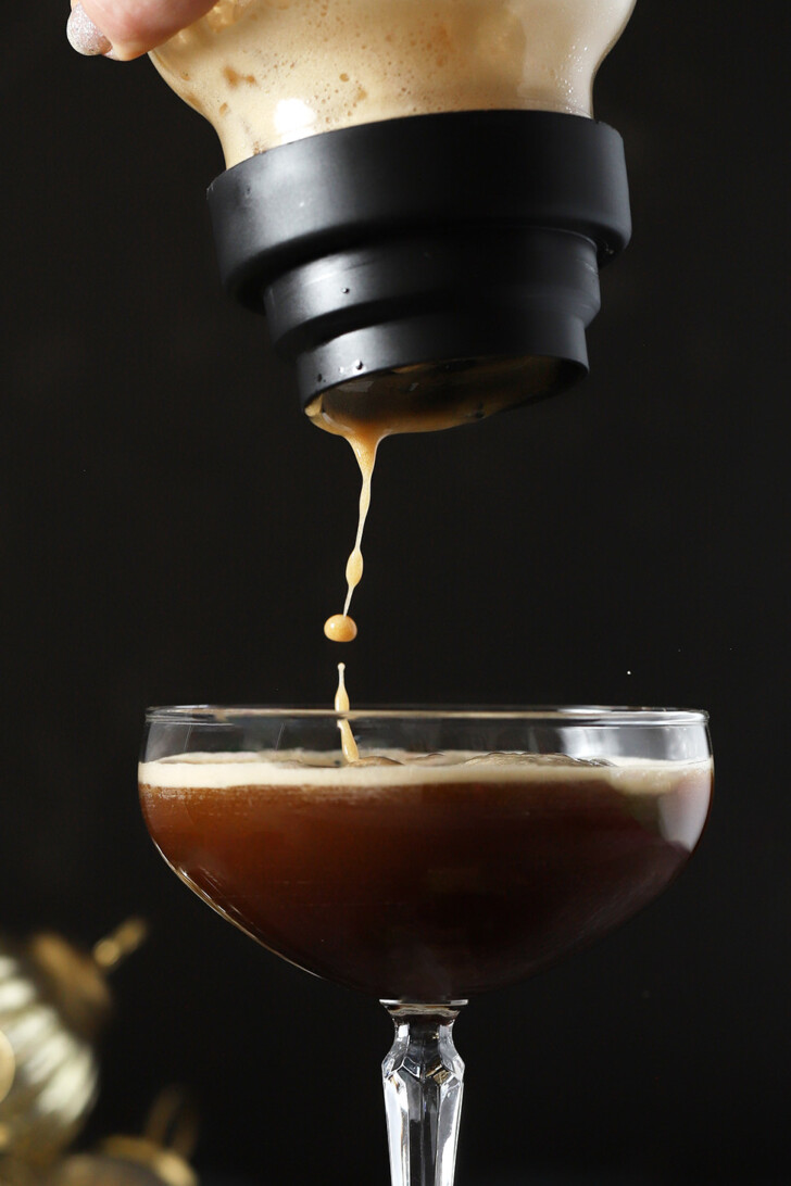 Gingerbread Espresso Martini being poured from a cocktail shaker into a coupe glass.
