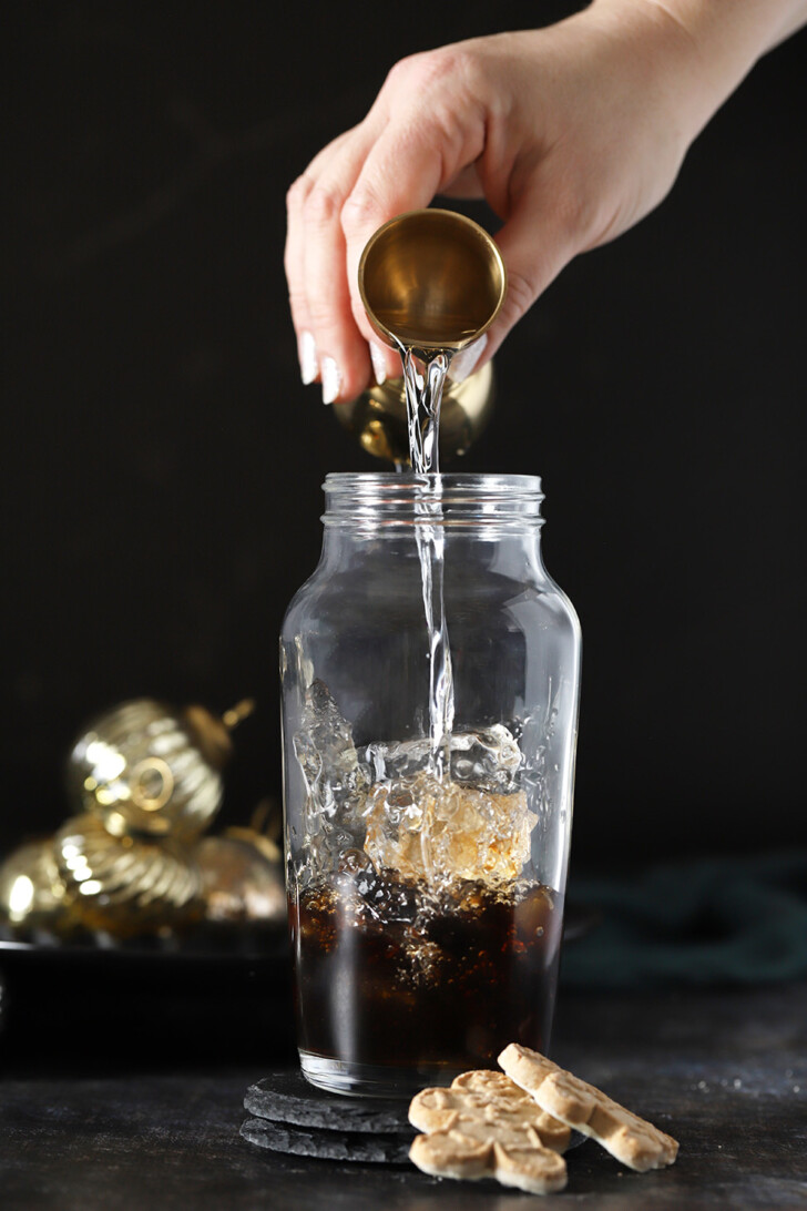 A hand pouring vodka into a cocktail shaker.