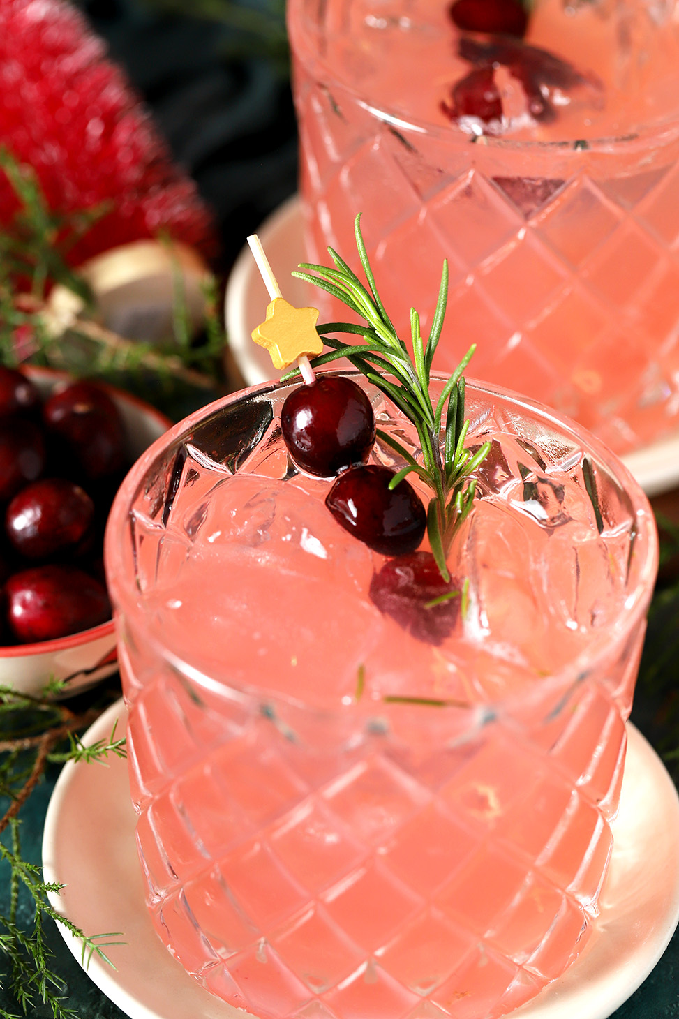 Glasses of Cranberry Mocktail garnished with a star cocktail pick with fresh cranberries and a sprig of rosemary.