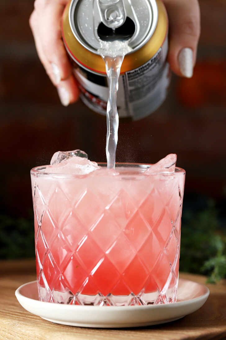 A hand pouring ginger beer into a glass filled with Christmas Cranberry Mocktail.