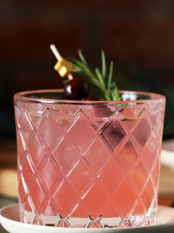 A glass of Cranberry Mocktail garnished with a star cocktail pick with fresh cranberries and a sprig of rosemary.