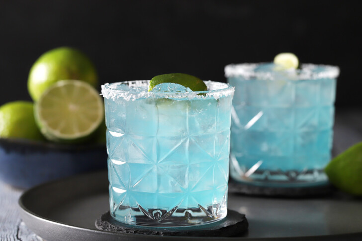 Blue margaritas with salted rims and lime garnishes.