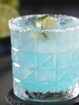 A blue margarita with a salted rim and a lime garnish.