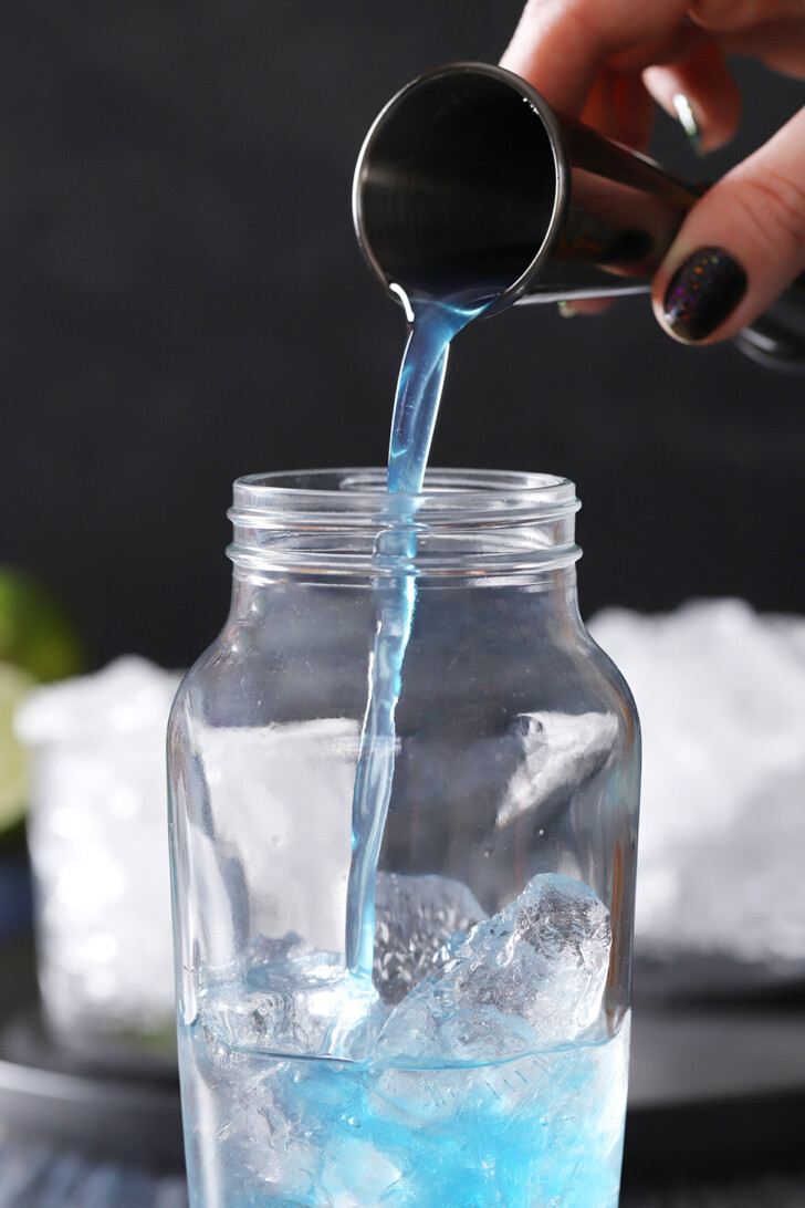 Blue curacao syrup being poured into a cocktail shaker.