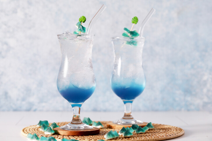 A pair of hurricane glasses filled with blue mocktail topped with gummy sharks.