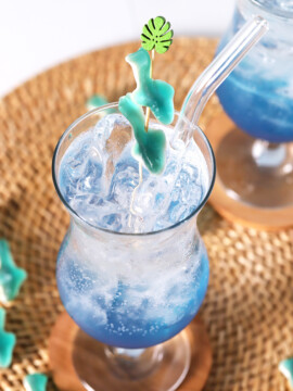 A hurricane glass filled with blue mocktail garnished with gummy sharks.