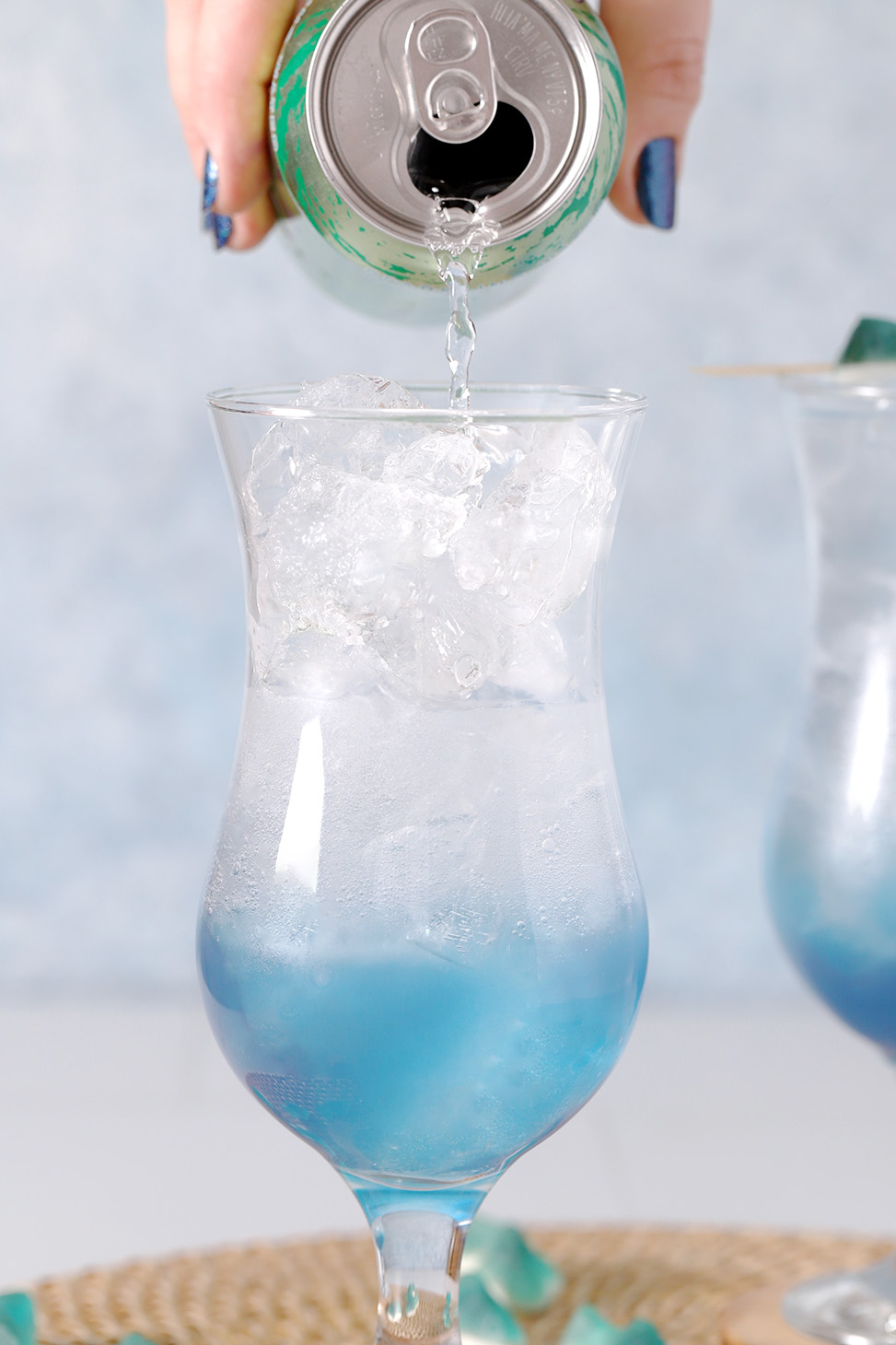 A hand pouring club soda into a hurricane glass filled with ice.