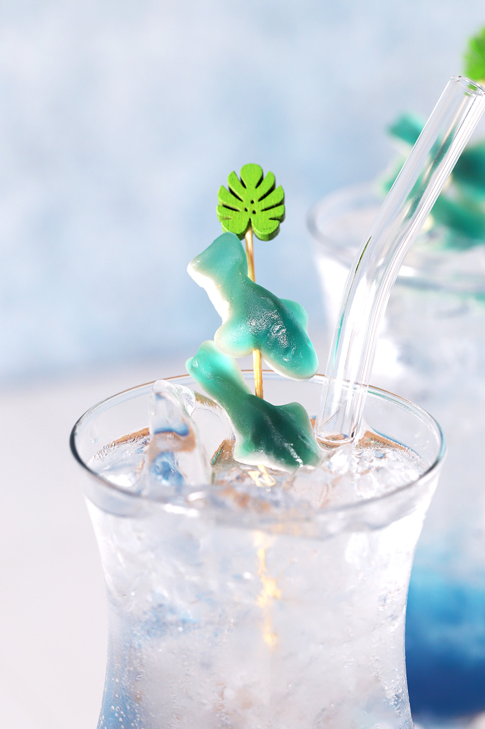 A pair of gummy sharks on a cocktail pick in a blue mocktail.