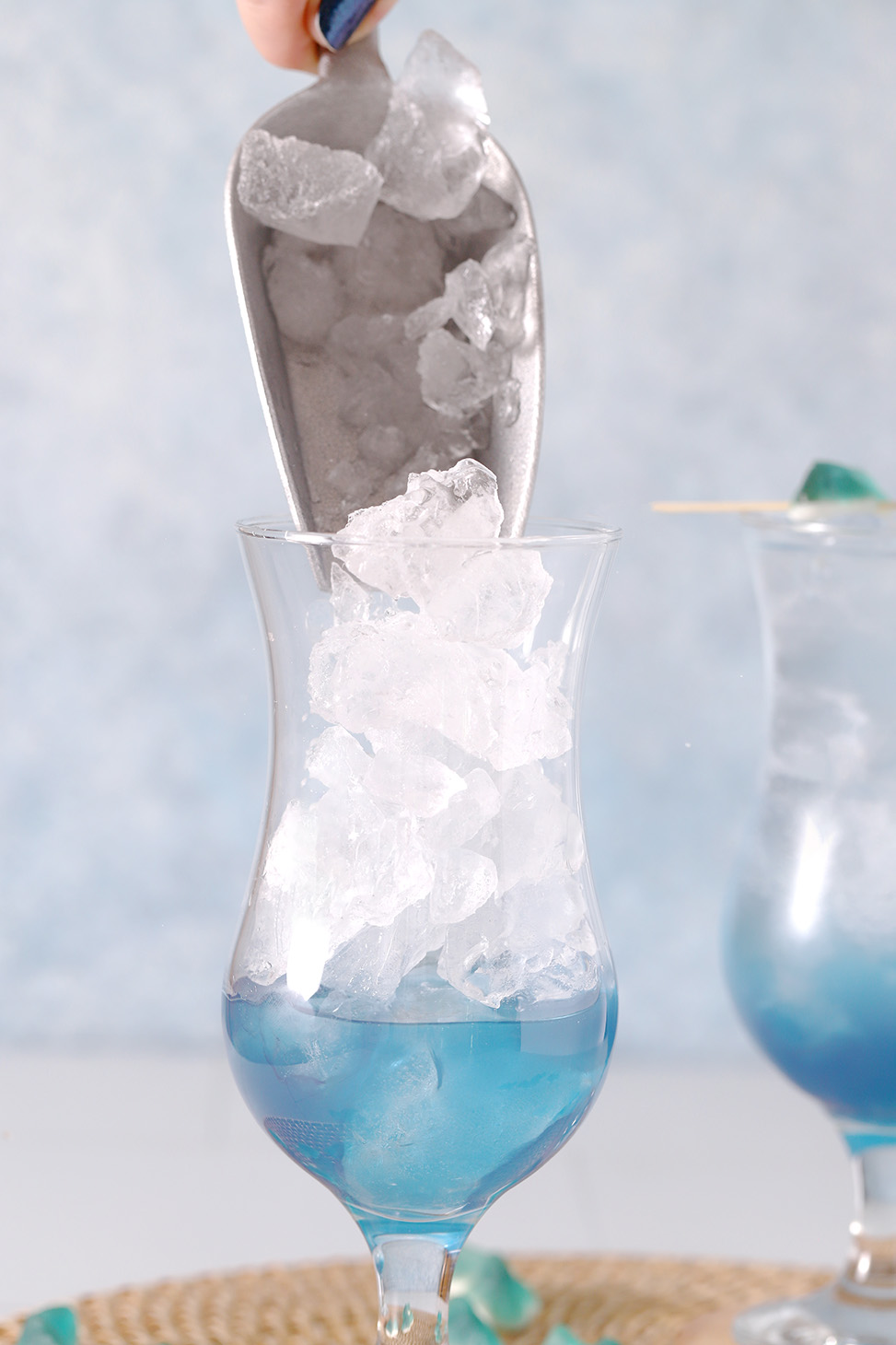 A silver scoop pouring ice into a hurricane glass.